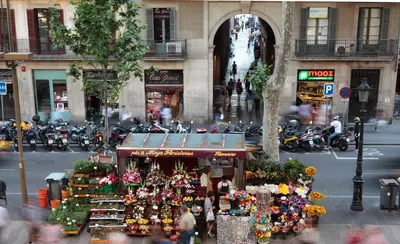 a flower market on a city street with people and motorcycles at Rambla 102 in Barcelona