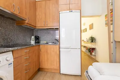 a white refrigerator in a kitchen with wooden cabinets at ApartEasy - Central Barcelona Studio Apartment in Barcelona