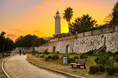 a building with a lighthouse in the distance with a bench at Sunset Bay Vilanova in Vilanova i la Geltrú