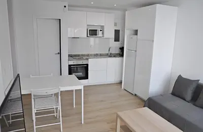 a white kitchen and living room with a table and a couch at Centro Sitges in Sitges