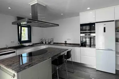 a kitchen with white cabinets and a counter with stools at Villa Oasis entre Viñedos cerca de Barcelona con A A y piscina climatizada in Caserío de Caʼn Rosell