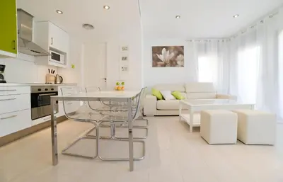 a white kitchen and living room with a table and chairs at Tranquil Duplex Sitges, sea views, private parking, terrace in Sitges