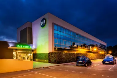 a building with two cars parked in a parking lot at B&B HOTEL Barcelona Sant Cugat in Sant Cugat del Vallès