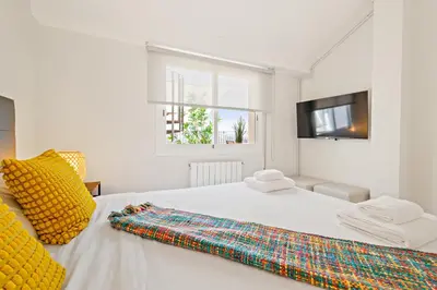 a white bedroom with a white bed with yellow pillows and a television at Tendency Apartments Sagrada Familia Penthouse in Barcelona
