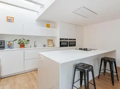 a white kitchen with white cabinets and black stools at Villa Alella Panoramic Views in Alella