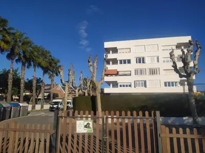 a tall white building with palm trees and a fence at Primera línea de mar y piscina a 20 minutos de Barcelona in Premiá de Mar