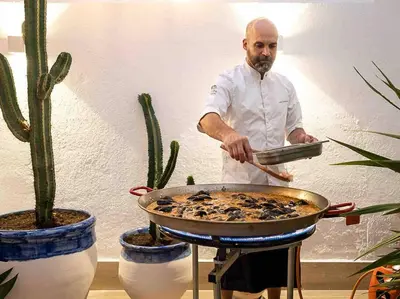 a man cooking food in a pan on a grill at Casa Mandarina: 4 Bedrooms - 2 Terraces - Parking in Hospitalet de Llobregat
