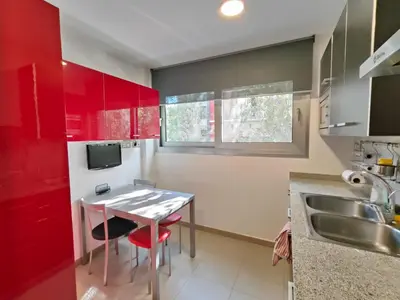 a kitchen with red cabinets and a table and a sink at Family apartment Forum in Sant Adria de Besos