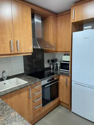 a kitchen with wooden cabinets and a white refrigerator at Acogedor apartamento Vallparadís con parking in Terrassa