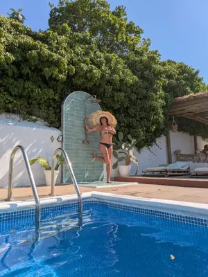 a woman in a hat standing next to a swimming pool at AMIRA home near Sitges in Sant Pere de Ribes