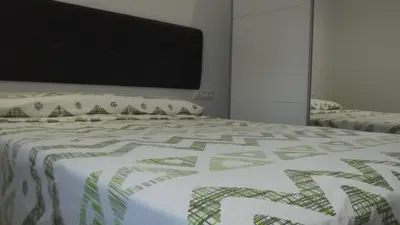 a bed with a green and white quilt on it at Apartamentos Atlas Terrassa I in Terrassa