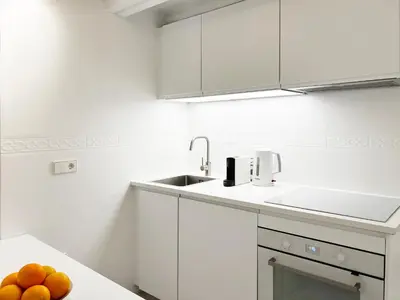 a white kitchen with a sink and oranges on a counter at White Apartment Barcelona in Barcelona
