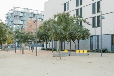 a park with trees and yellow chairs in front of a building at Canela Homes BARCELONA PARK GÜELL in Barcelona