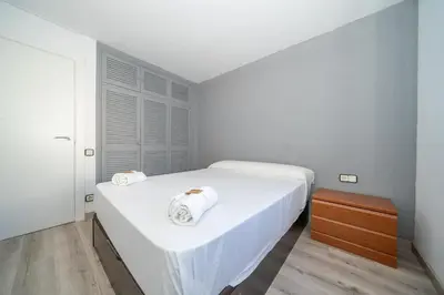 a white bedroom with two beds and a wooden table at HomeHolidaysRentals Deva - Costa Barcelona in Pineda de Mar