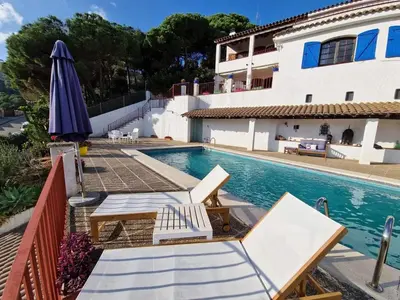 a swimming pool with chairs and an umbrella next to a house at Villa Alella, 5 bedrooms & pool in Alella