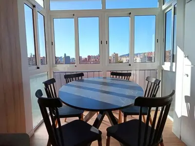 a blue table and chairs in a room with windows at Ático cerca Playa y centro a 10 min. in Sant Adria de Besos