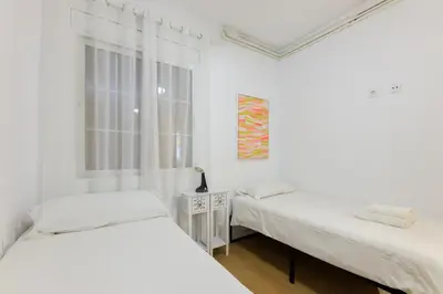a white bedroom with two beds and a window at ApartEasy - Private terrace, 3 bedrooms, Eixample in Barcelona