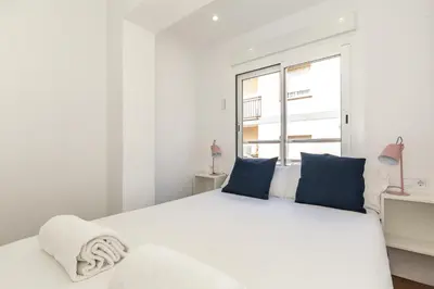 a white bedroom with a large white bed with blue pillows at Picasso Suites Cornellá in Cornellà de Llobregat
