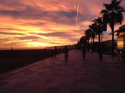 a group of people riding bikes down a sidewalk at sunset at Lets Holidays Castelldefels Diagonal Orient in Castelldefels