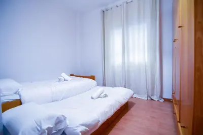 two beds in a room with white walls and wood floors at Touch the Sky in Hospitalet de Llobregat