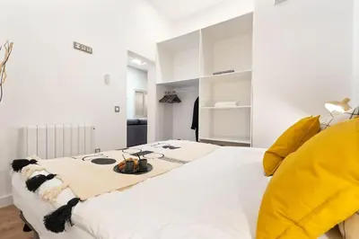 a white bedroom with a large white bed with yellow pillows at Enamorats Glorias in Barcelona