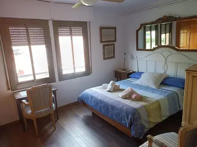 a bedroom with a bed and a chair and two windows at Apartamento al lado de Barcelona y la playa in Montgat