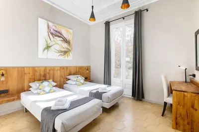 two beds in a room with a desk and a window at Jardinets Guest House in Barcelona
