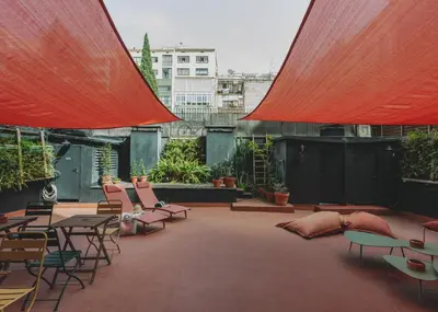a rooftop patio with chairs and tables and red umbrellas at Piulet Hostel in Barcelona