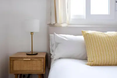 a bed with a pillow and a nightstand next to a window at Amazing 3bdr Apt In Cornella 1 Mins From Metro in Cornellà de Llobregat
