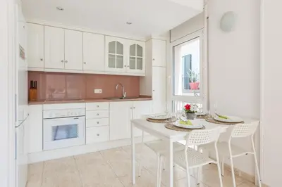 a kitchen with white cabinets and a white table and chairs at Nova Apartment by Hello Homes Sitges in Sitges