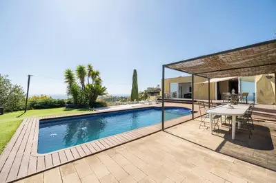 a swimming pool with a table and a house at Casa Mar Blava con piscina comunitaria junto Barcelona Centro in Alella