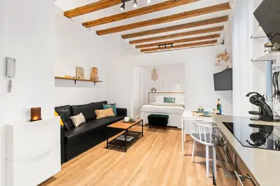 a living room with a black couch and a kitchen at Lodging Apartments Almirall Beach 11 in Barcelona