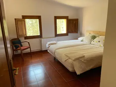 a bedroom with a bed and a chair and two windows at Casa rural El Bruguer Vell in Santa Eulalia de Ronsaná