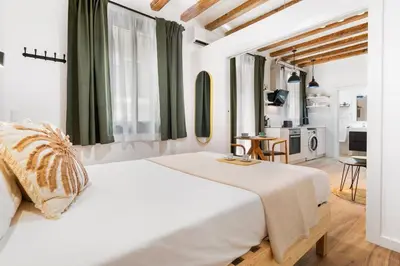 a bedroom with a large white bed and a kitchen at Lodging Apartments Almirall Beach 21 in Barcelona
