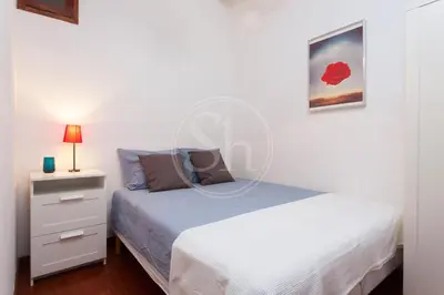 a white bedroom with a bed and a night stand at Tranquilo y luminoso apartamento en el Eixample in Barcelona