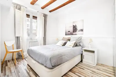 a white bedroom with a bed and a chair at Charming Beachside Apartment in Barceloneta in Barcelona