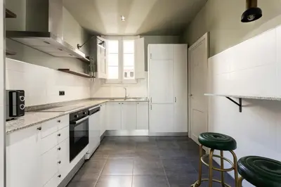 a kitchen with white cabinets and green stools in it at Spacious Stylish 4-bedroom Modernist Apartment in Barcelona