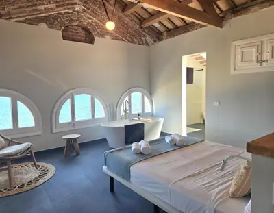 a bedroom with a bed and a tub and windows at Casa Mas Blau | Increíbles vistas frente al mar in San Pol de Mar