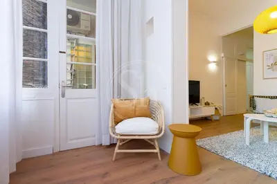 a living room with a chair and a yellow stool at Cómodo piso en Eixample in Barcelona
