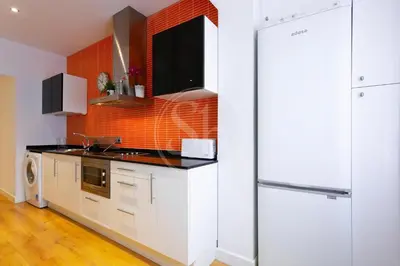 a kitchen with white cabinets and an orange tile wall at Bonito apartamento cerca de la Sagrada Familia in Barcelona