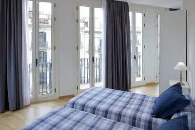 a bedroom with a bed with blue pillows and windows at Flateli Pelayo H1 in Barcelona