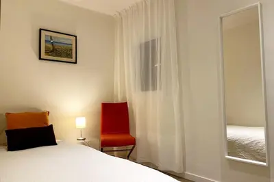 a bedroom with a bed and a red chair and a window at Bright airy family style 7 min walk to beach in Caldes d'Estrac