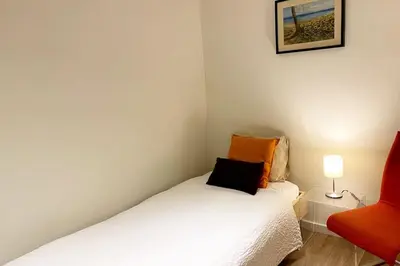 a small bedroom with a bed and a red chair at Bright airy family style 7 min walk to beach in Caldes d'Estrac
