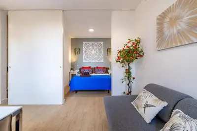a living room with a blue couch and a bed at Modern Apartment 2 rooms 15' Bcn Center - Fira Barcelona in Barcelona