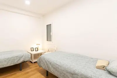 a white bedroom with two beds and a table at Lindo apartamento Montjuïc in Barcelona