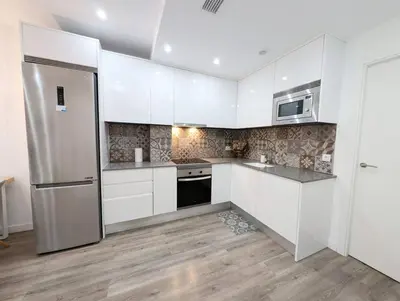 a kitchen with white cabinets and a stainless steel refrigerator at New flat in the centre, 10 min from BCN Airport in Cornellà de Llobregat