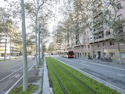 a red bus driving down a city street with trees at Winahost Barcelona Diagonal in Barcelona