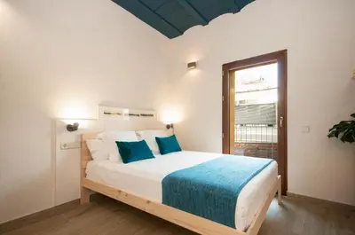 a white bedroom with a large bed with blue sheets at ecoGrusApartments in Masnou