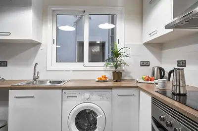a white kitchen with a washing machine and a window at Spacious 3BRapartment in PobleSec with balcony in Barcelona