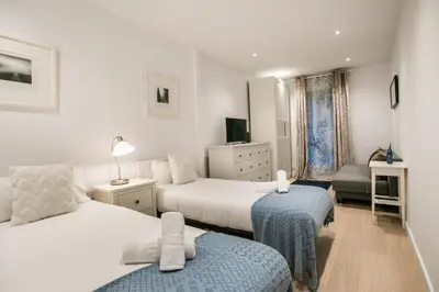 a white bedroom with two beds and a chair at E4lle1031 - Studio next to Plaza Espanya in Barcelona